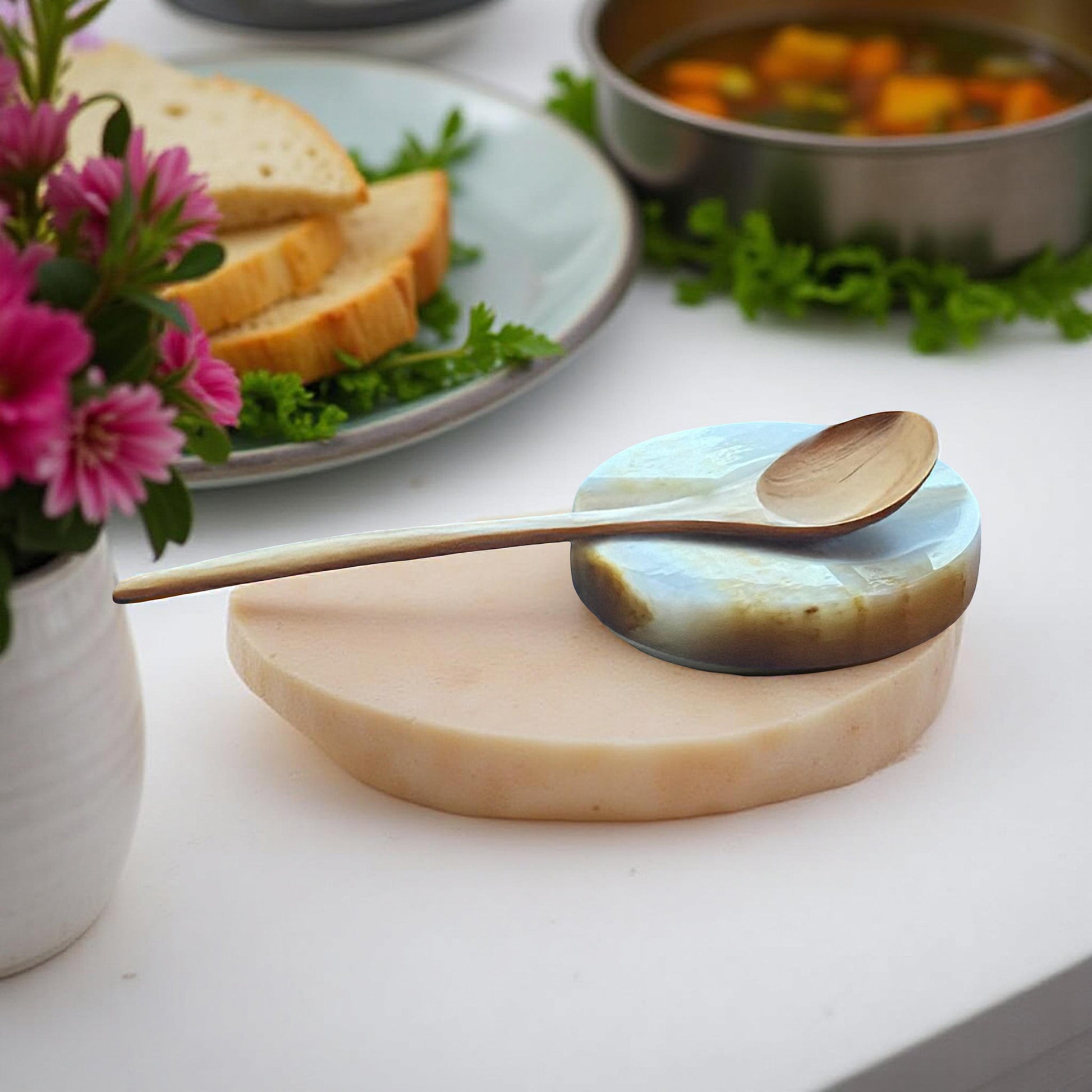 Onyx spoon rest with wooden spoon beside soup and sliced bread