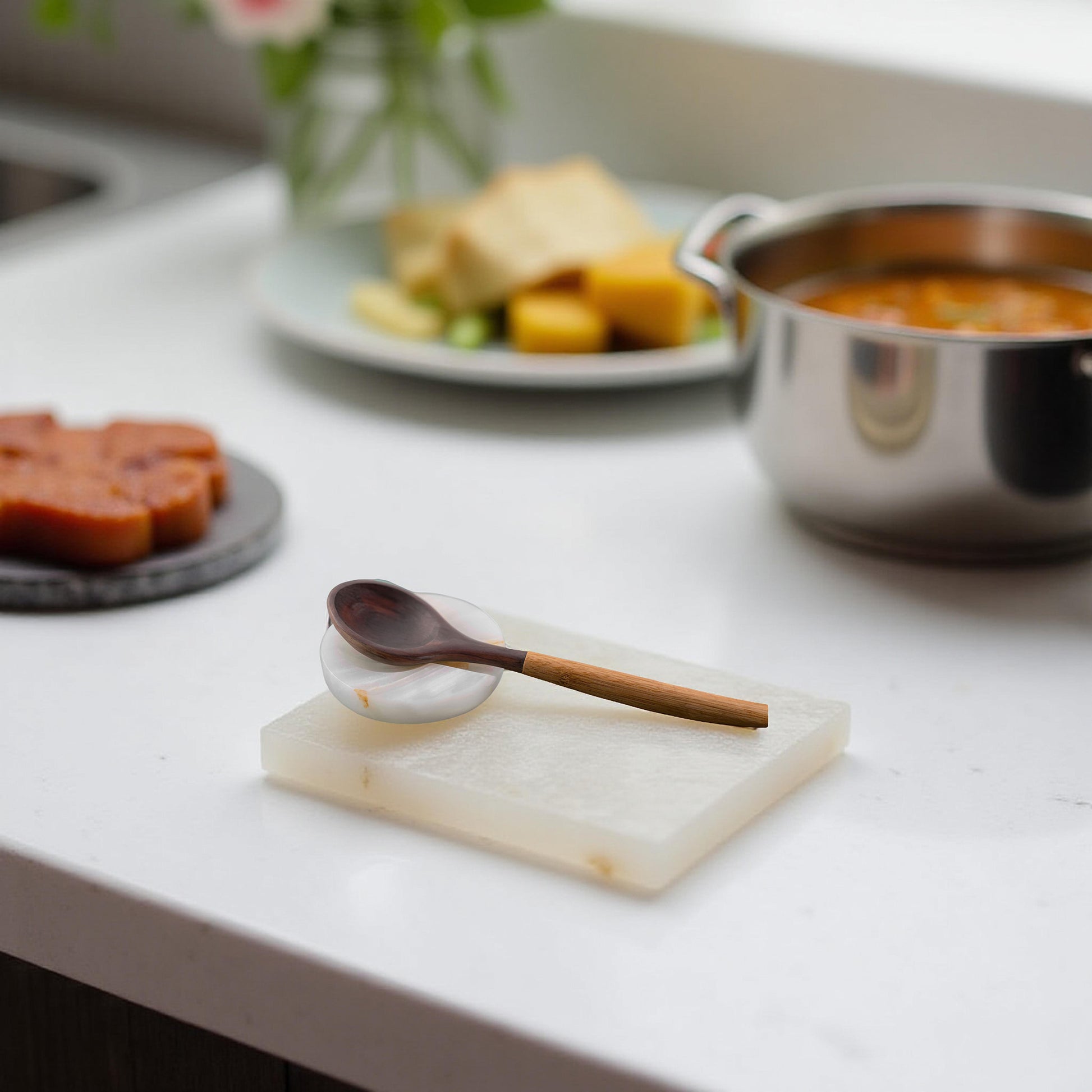 Onyx spoon rest with wooden spoon beside stainless steel pot in a clean kitchen